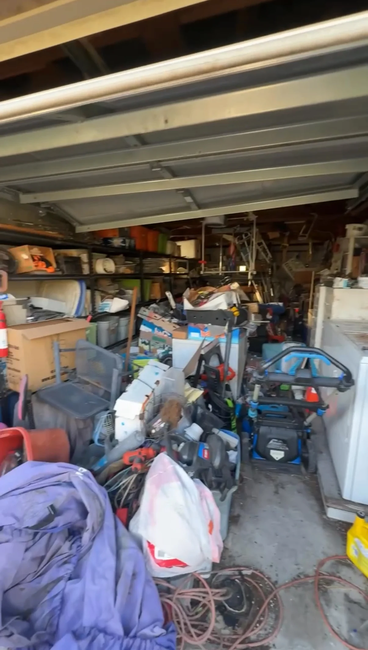Garage packed with boxes, shelving, yard equipment and household clutter before a cleanout.